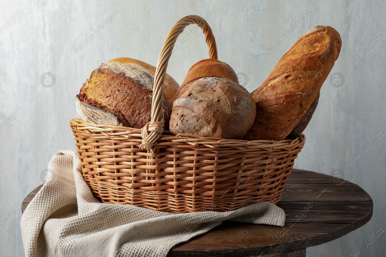 Photo of Different freshly baked bread loafs in wicker basket on wooden table, closeup