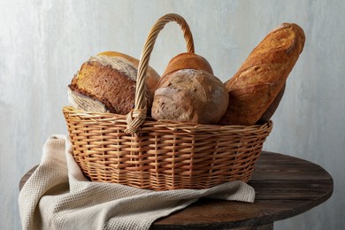 Photo of Different freshly baked bread loafs in wicker basket on wooden table, closeup