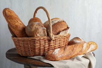 Photo of Different freshly baked bread loafs and wicker basket on wooden table, closeup