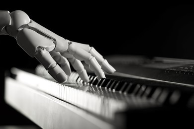 Photo of Artificial intelligence. Robot hand playing synthesizer on black background, closeup