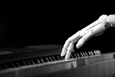 Photo of Artificial intelligence. Robot hand playing piano on black background, closeup