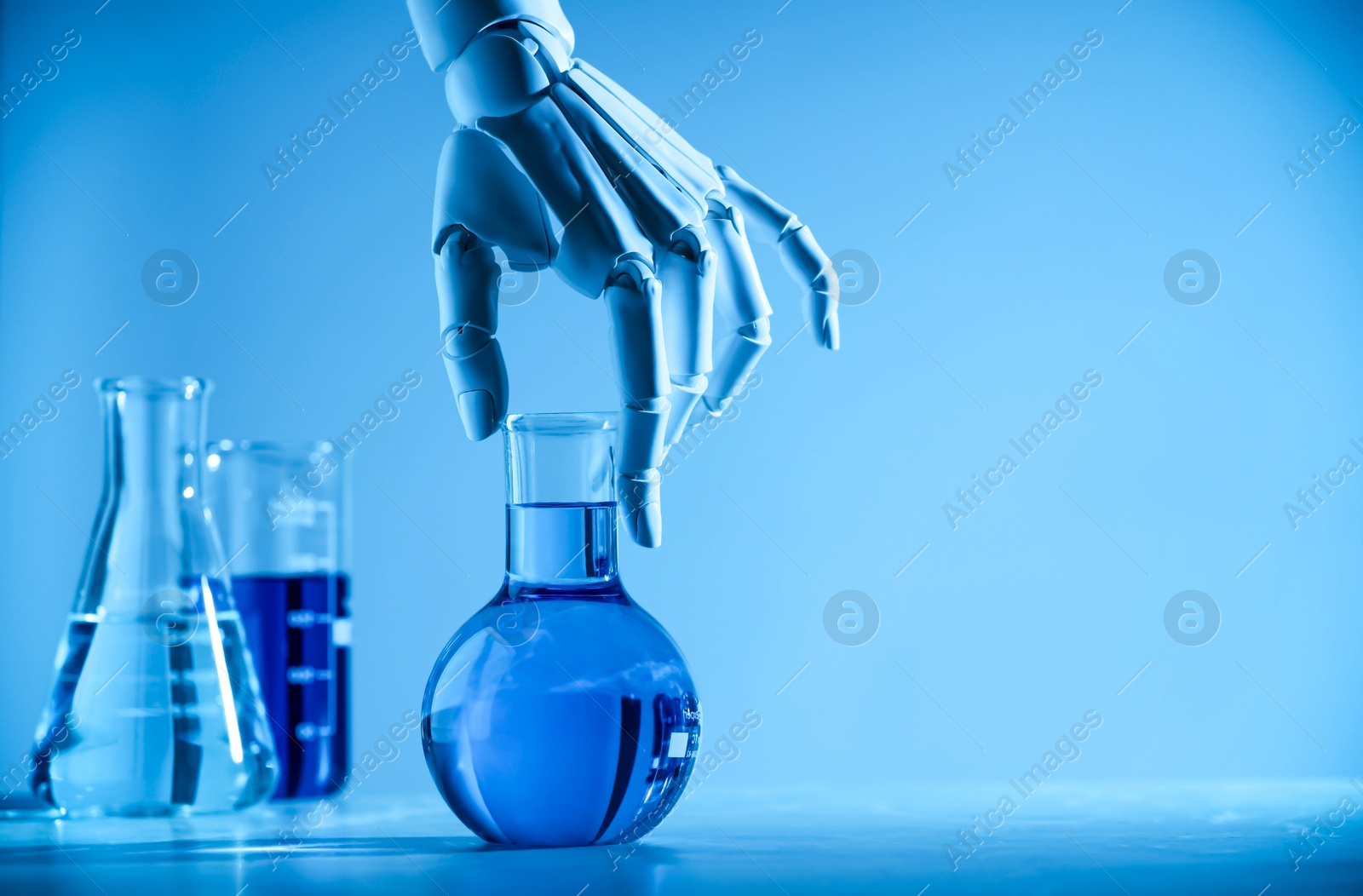 Photo of Artificial intelligence. Robot hand with flask at table in blue light, space for text