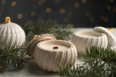 Photo of Soy wax candles and green fir branches on white marble table, closeup. Beautiful Christmas decor