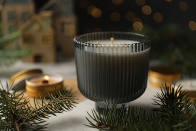 Soy candle and green fir branches on white table, closeup