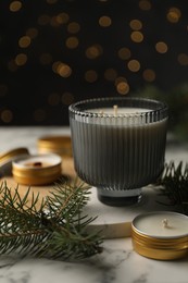 Photo of Soy candles and green fir branches on white marble table, closeup