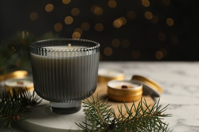 Photo of Soy candles and green fir branches on white marble table, closeup. Space for text