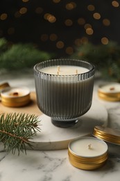 Photo of Soy candles and green fir branches on white marble table, closeup