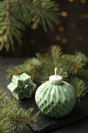 Photo of Soy candles in shape of snowflake and Christmas ball among green fir branches on grey table, closeup