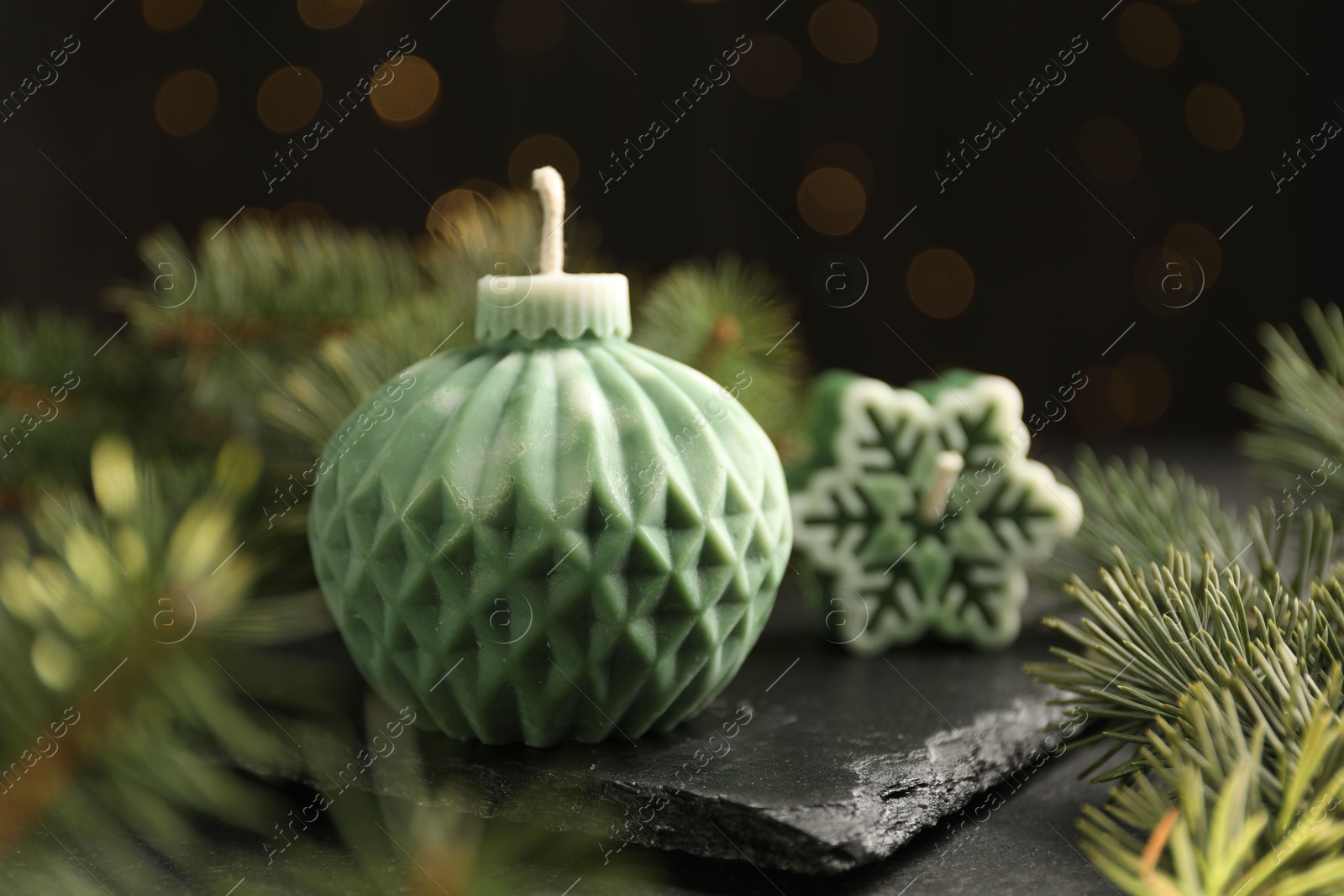 Photo of Soy candles in shape of snowflake and Christmas ball among green fir branches on grey table, closeup