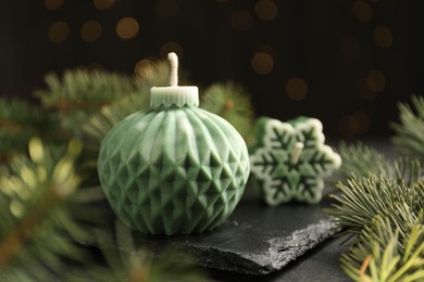 Photo of Soy candles in shape of snowflake and Christmas ball among green fir branches on grey table, closeup