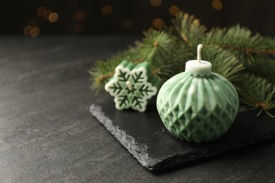 Photo of Soy candles in shape of snowflake and Christmas ball among green fir branches on grey table, closeup. Space for text