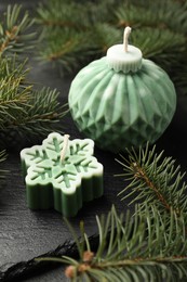 Photo of Soy candles in shape of snowflake and Christmas ball among green fir branches on grey table, closeup