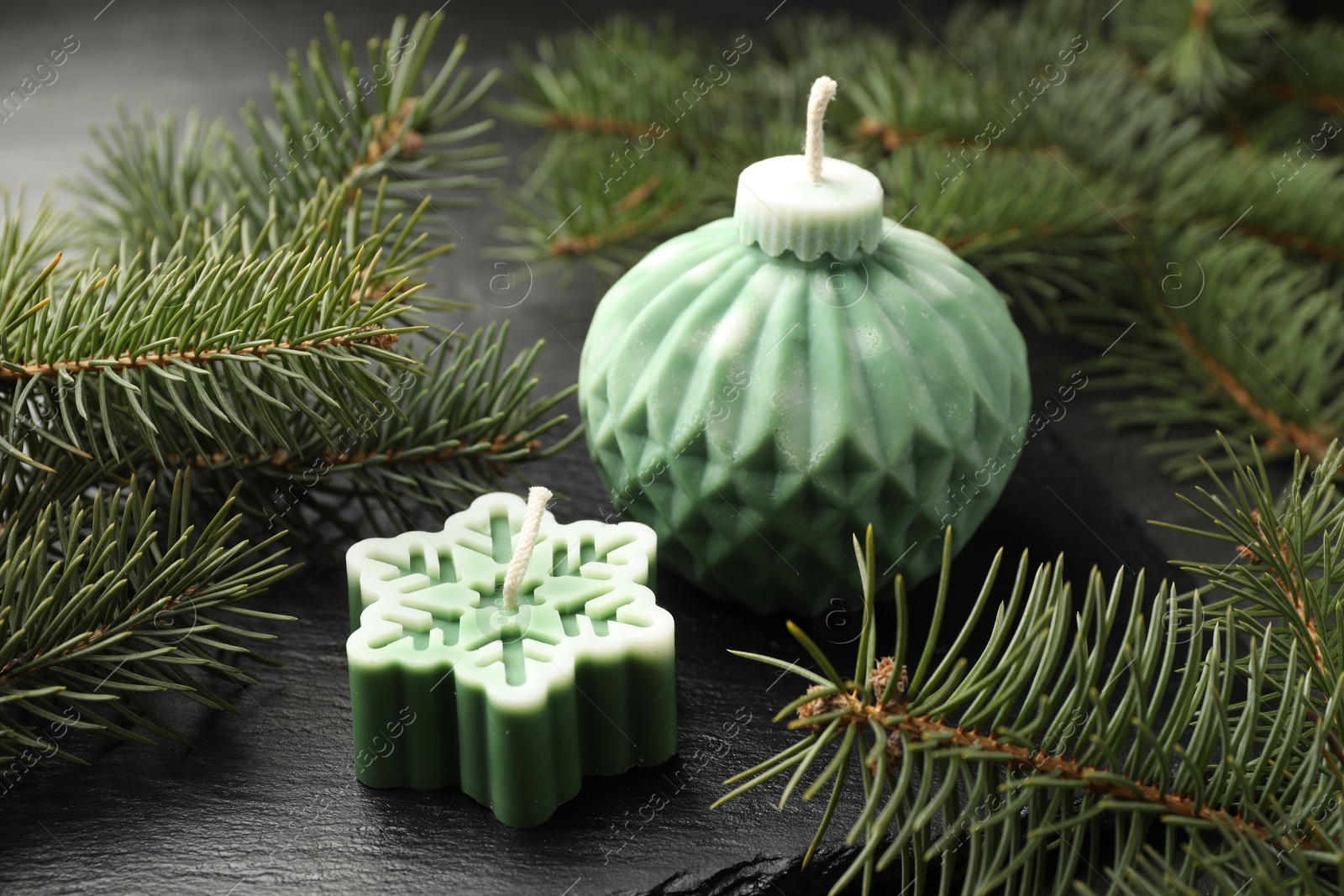 Photo of Soy candles in shape of snowflake and Christmas ball among green fir branches on grey table, closeup