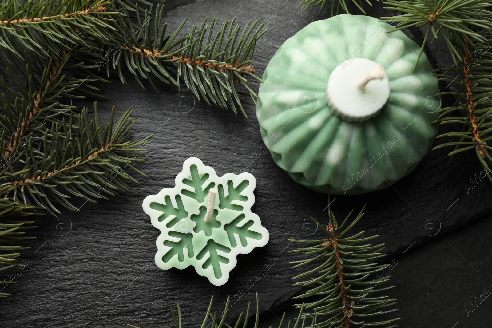 Photo of Soy candles in shape of snowflake and Christmas ball among green fir branches on grey table, flat lay