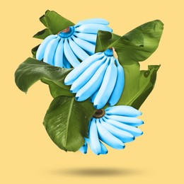 Image of Light blue bananas and green leaves in air on yellow background