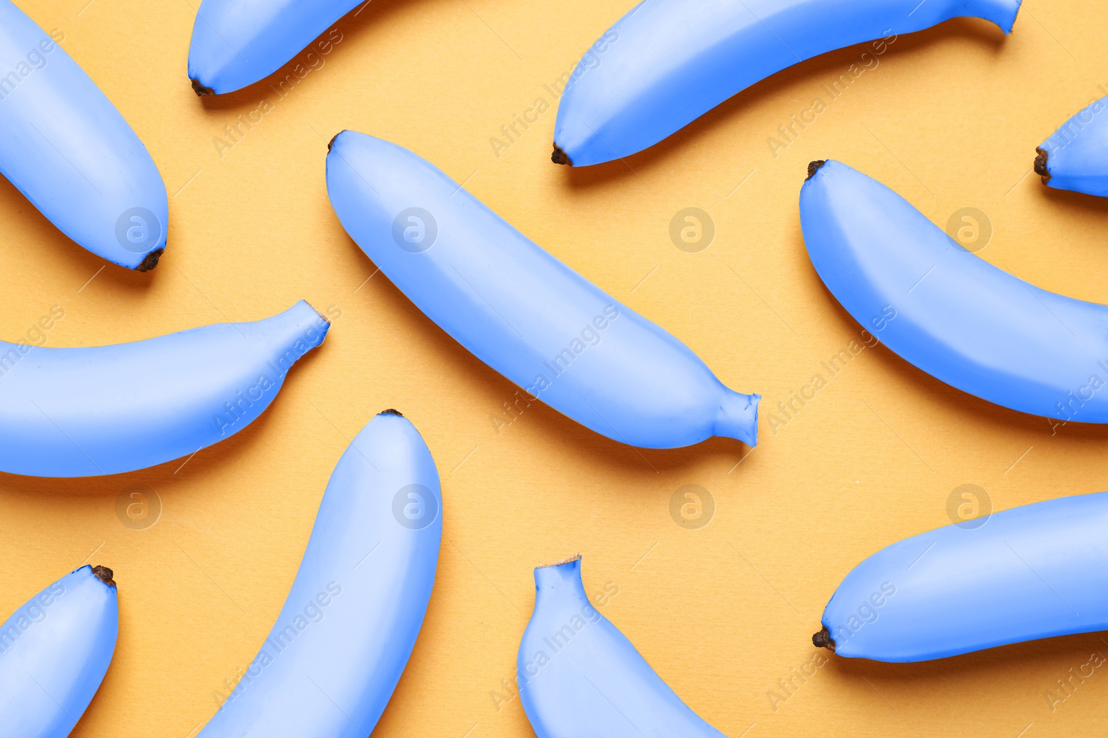 Image of Light blue bananas on pale orange background, flat lay