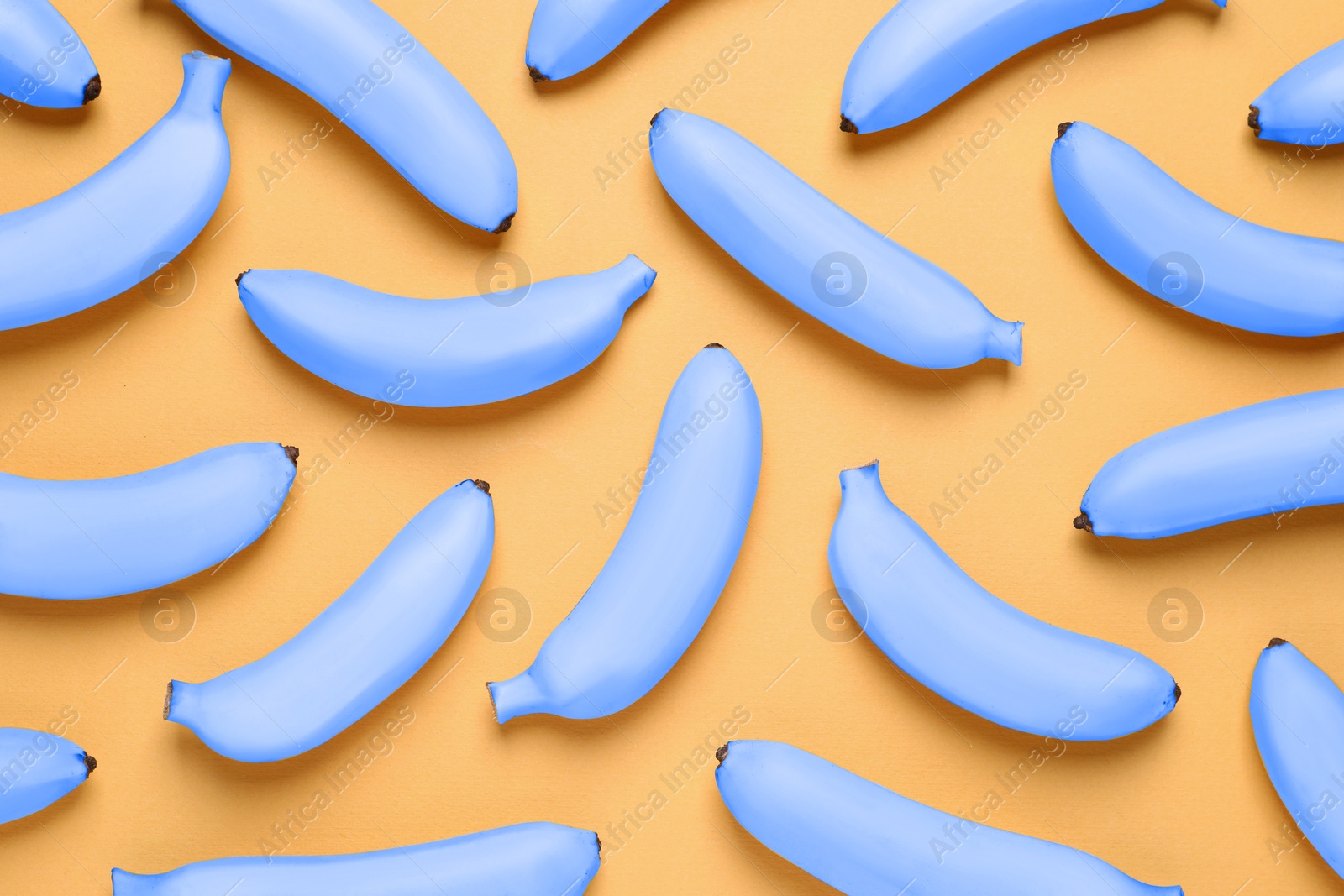 Image of Light blue bananas on pale orange background, flat lay