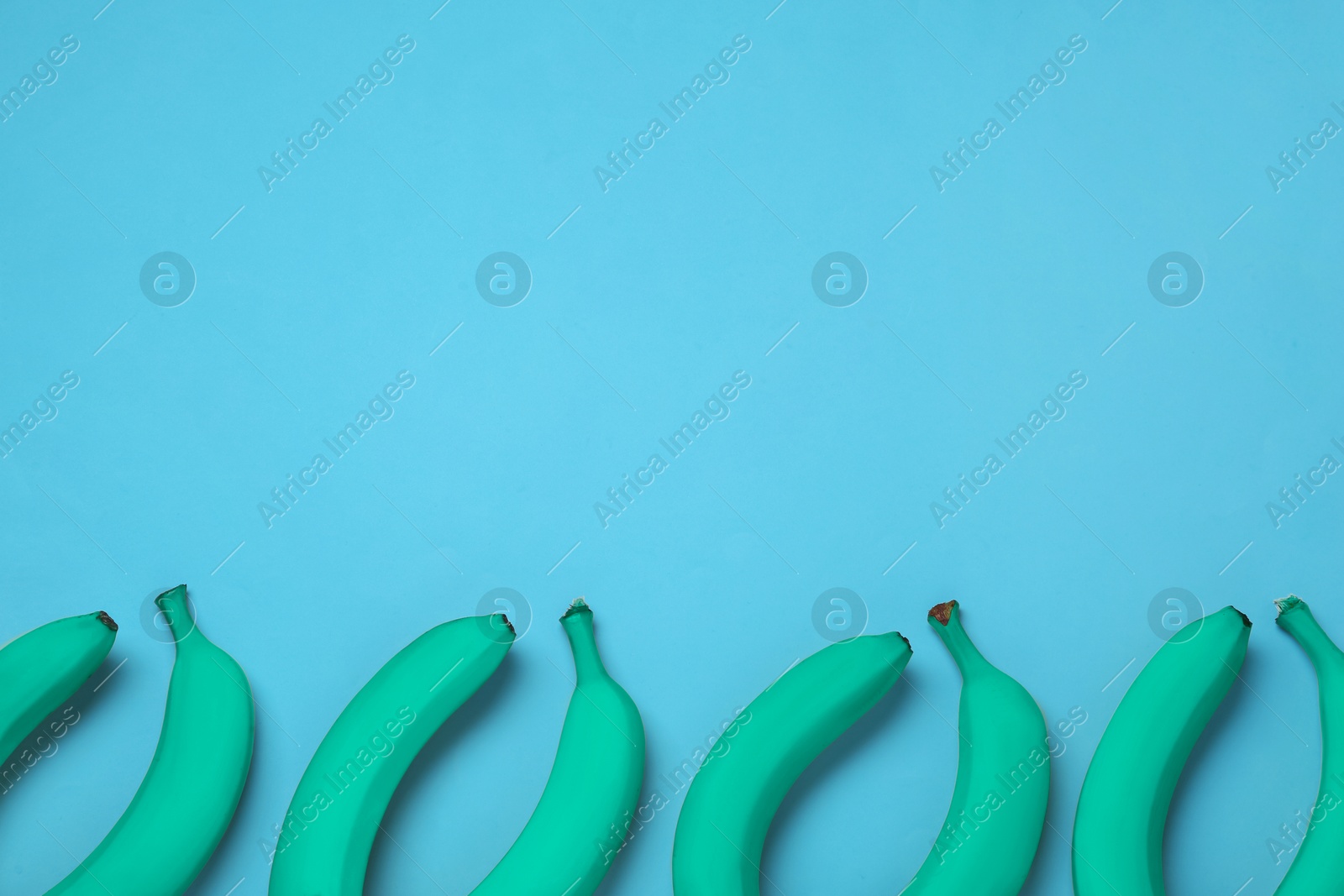 Image of Turquoise bananas on light blue background, flat lay. Space for text