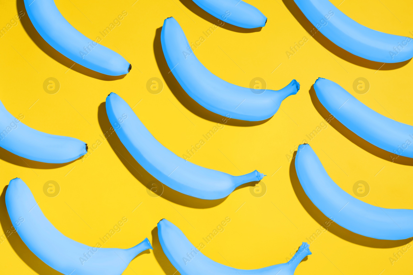 Image of Light blue bananas on yellow background, flat lay