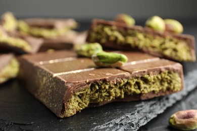 Photo of Pieces of Dubai chocolate bar with pistachios and knafeh on grey table, closeup