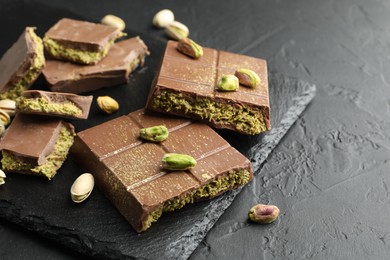 Photo of Pieces of Dubai chocolate bars with pistachios and knafeh on grey table, closeup. Space for text