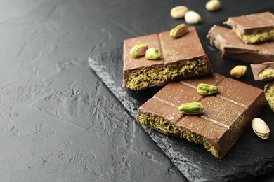 Photo of Pieces of Dubai chocolate bars with pistachios and knafeh on grey table, closeup. Space for text