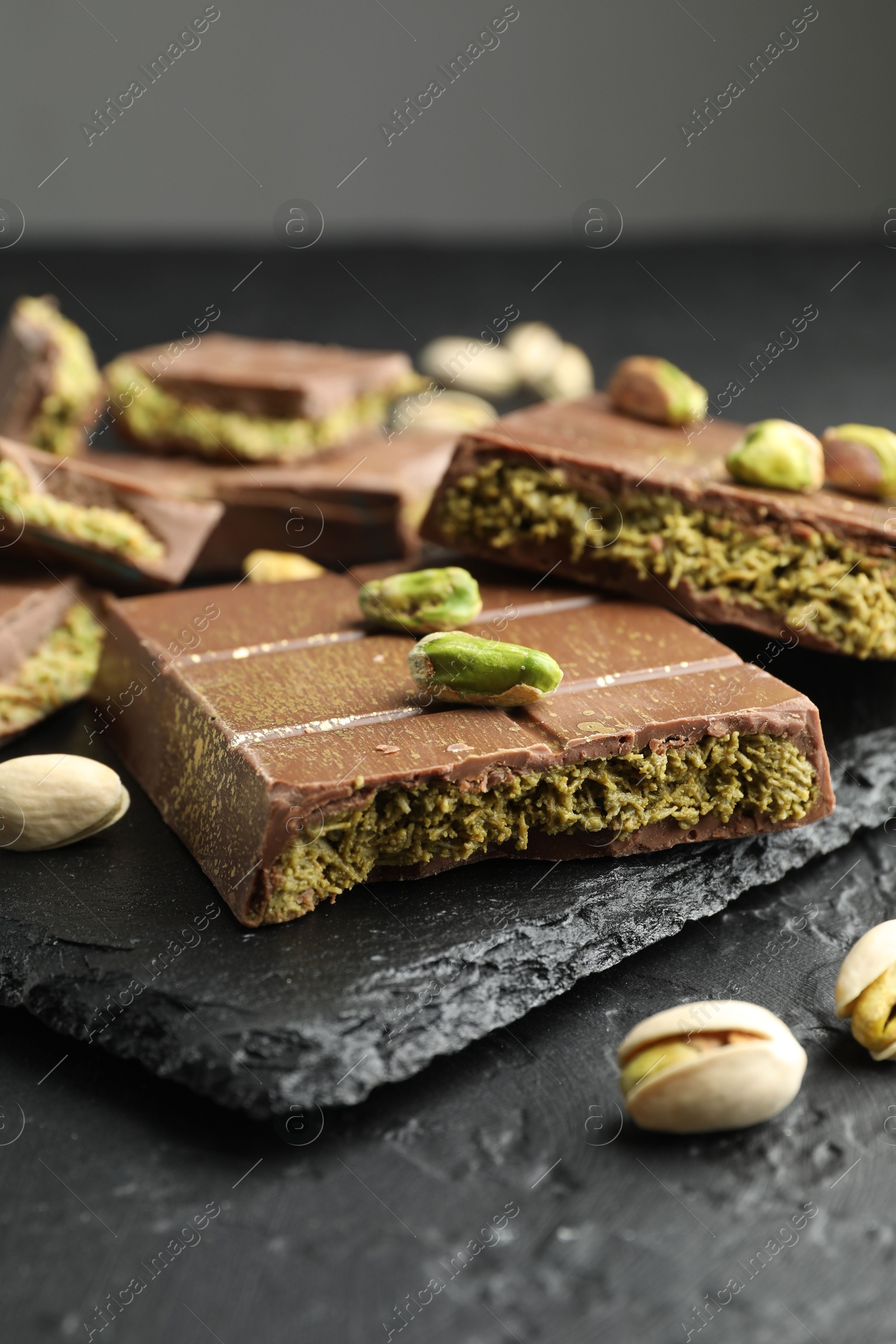 Photo of Pieces of Dubai chocolate bars with pistachios and knafeh on grey table, closeup