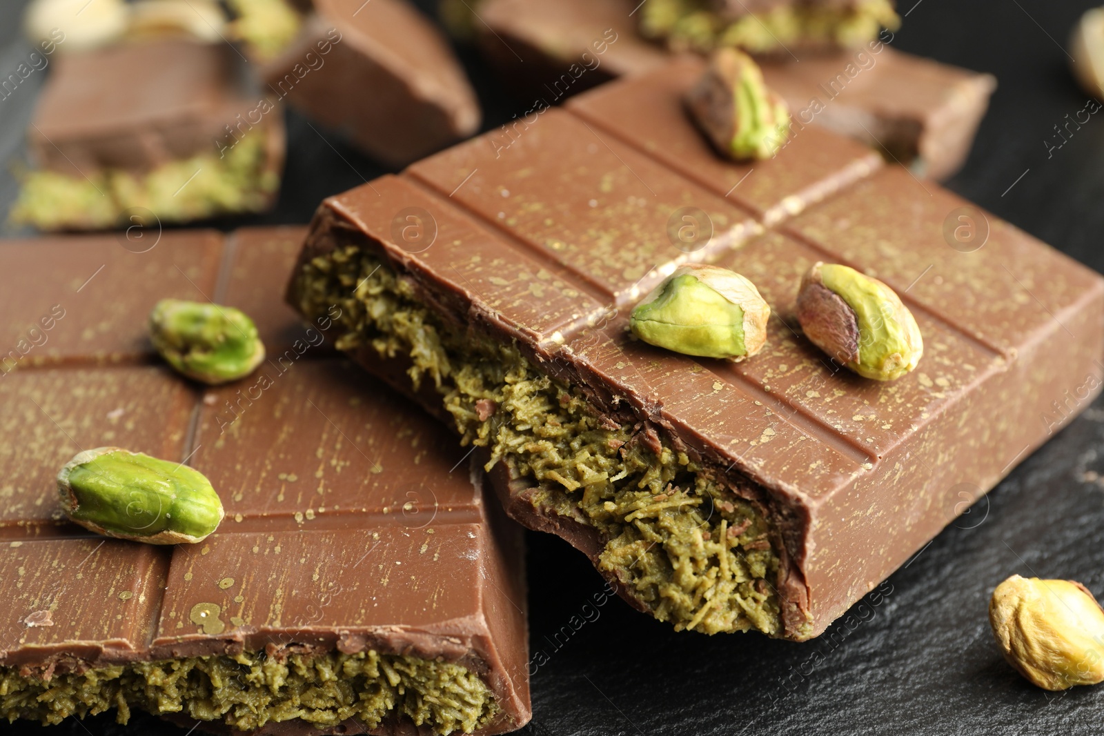 Photo of Pieces of Dubai chocolate bar with pistachios and knafeh on grey table, closeup