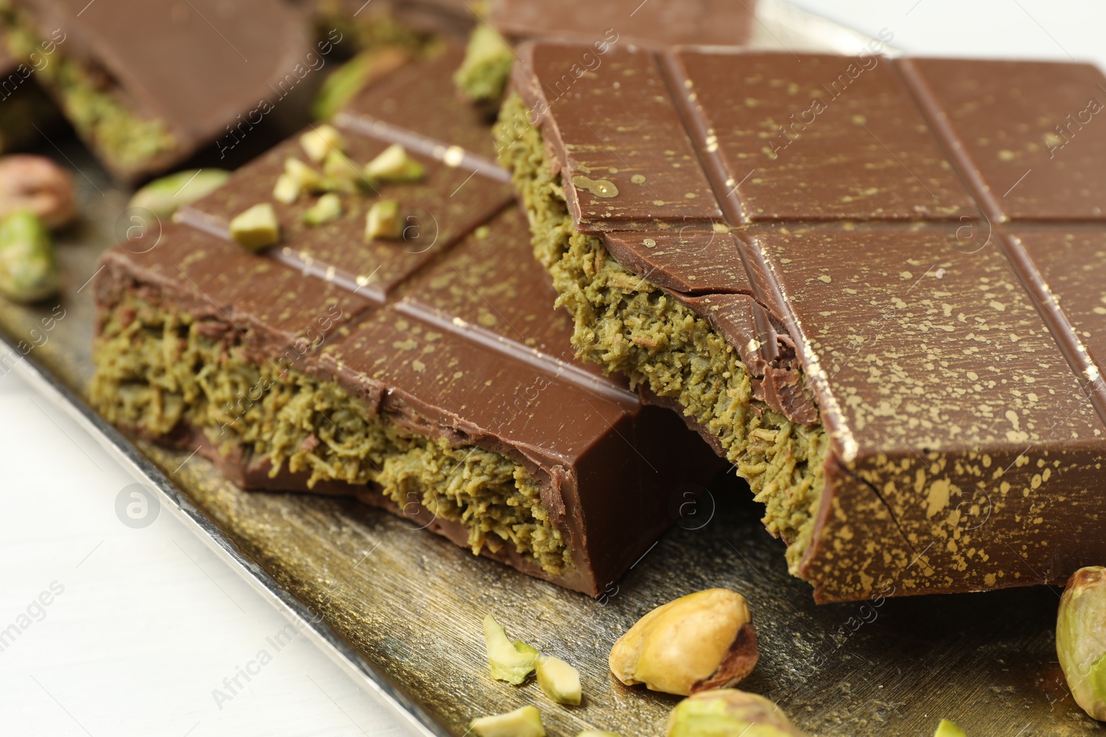 Photo of Pieces of Dubai chocolate bars with pistachios and knafeh on white table, closeup