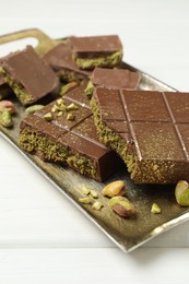 Photo of Pieces of Dubai chocolate bars with pistachios and knafeh on white wooden table, closeup