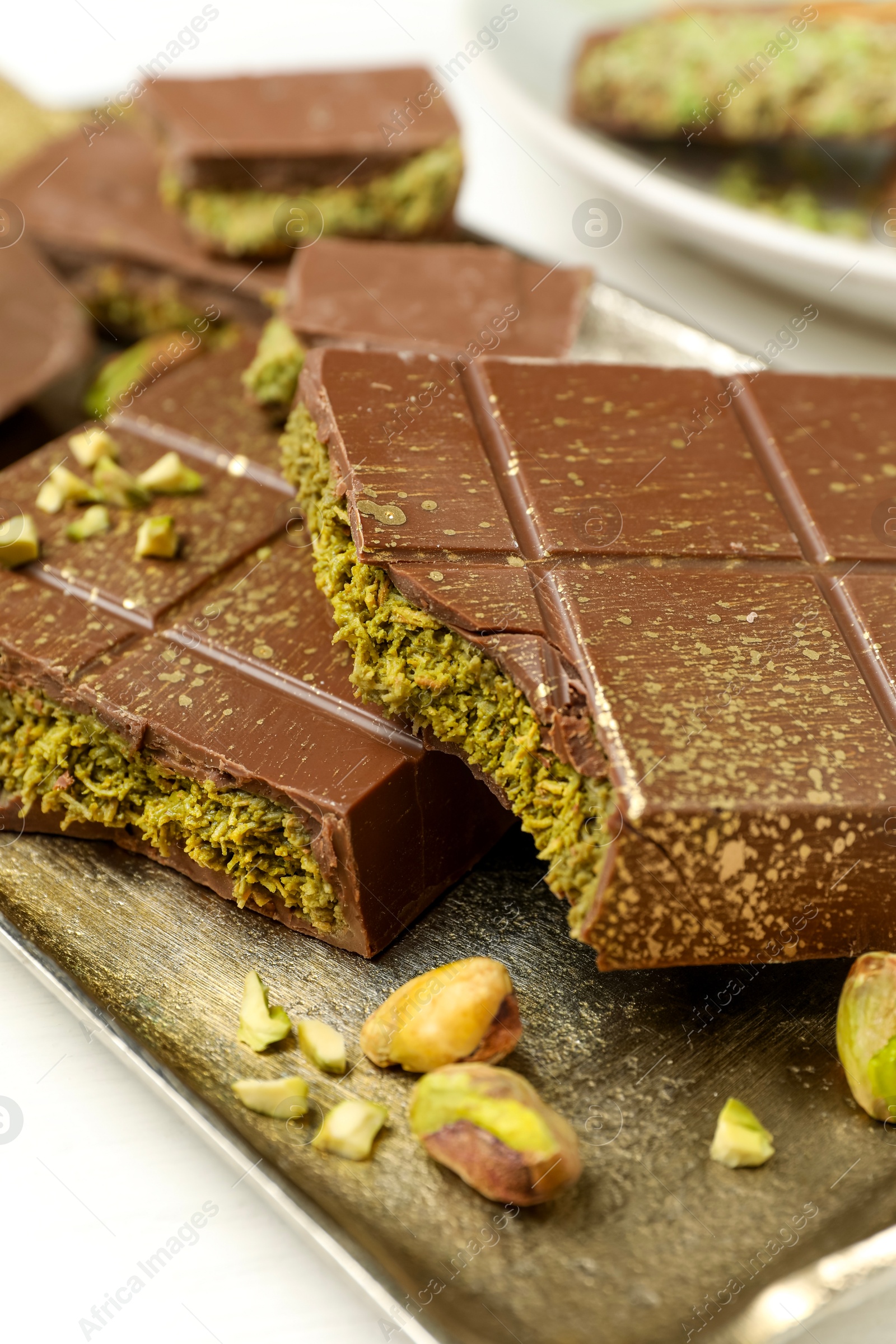 Photo of Pieces of Dubai chocolate bars with pistachios and knafeh on white table, closeup