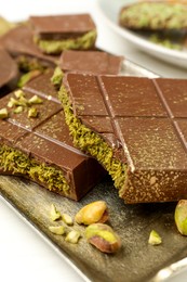 Photo of Pieces of Dubai chocolate bars with pistachios and knafeh on white table, closeup