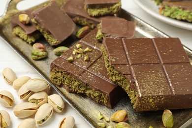 Photo of Pieces of Dubai chocolate bars with pistachios and knafeh on white table, closeup