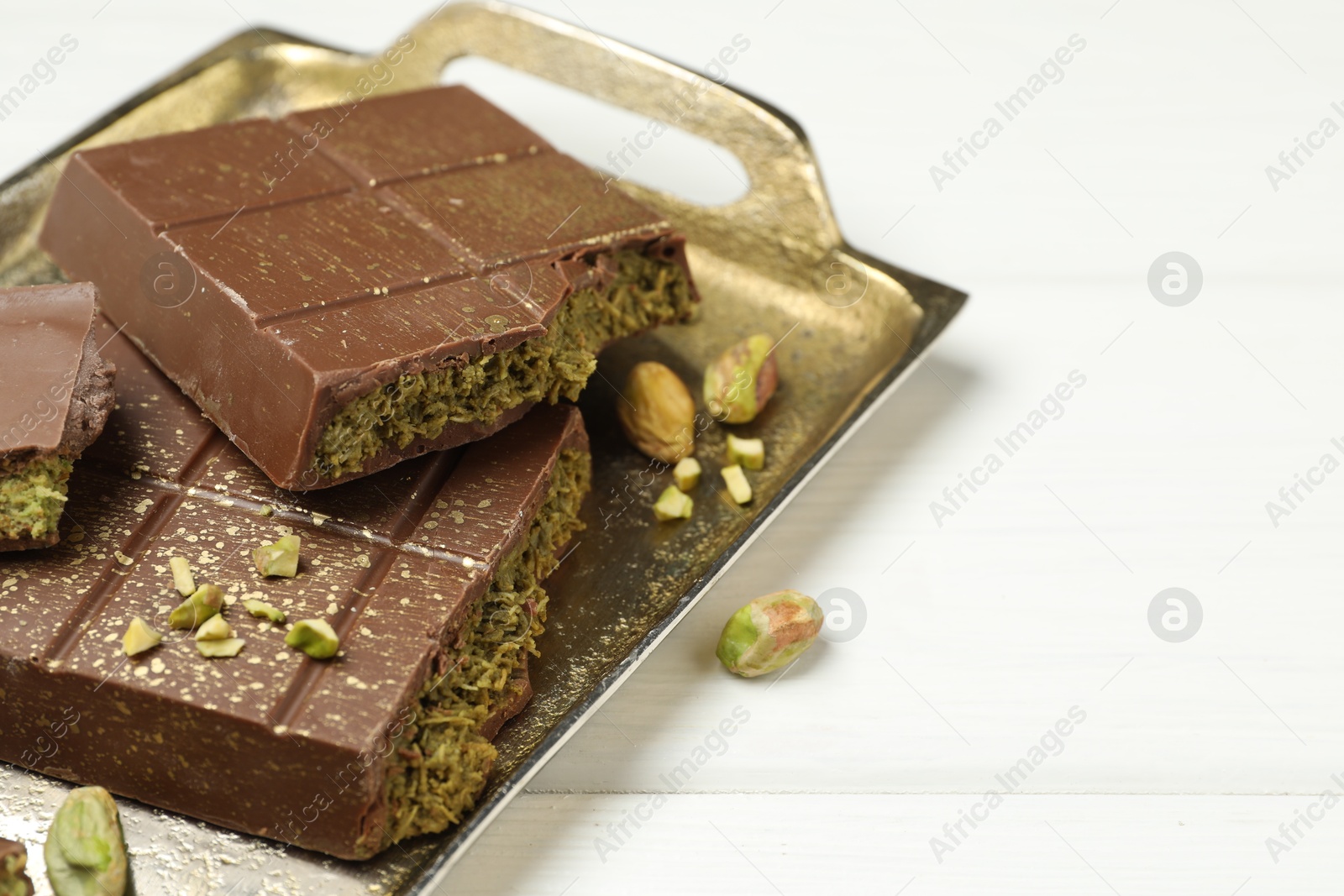 Photo of Pieces of Dubai chocolate bar with pistachios and knafeh on white wooden table, closeup. Space for text