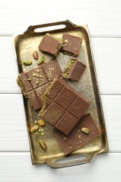 Photo of Pieces of Dubai chocolate bars with pistachios and knafeh on white wooden table, top view