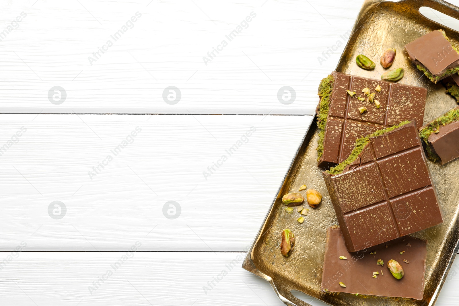 Photo of Pieces of Dubai chocolate bars with pistachios and knafeh on white wooden table, top view. Space for text