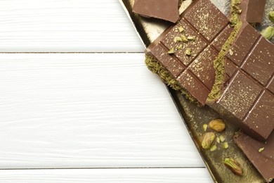 Photo of Pieces of Dubai chocolate bars with pistachios and knafeh on white wooden table, top view. Space for text