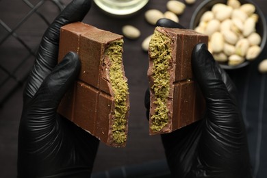 Photo of Woman breaking Dubai chocolate bar with pistachio and knafeh at table, closeup