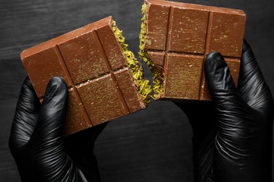 Photo of Woman breaking Dubai chocolate bar with pistachio and knafeh at dark table, closeup