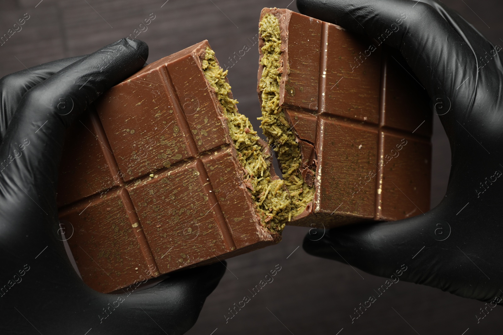 Photo of Woman breaking Dubai chocolate bar with pistachio and knafeh at dark table, closeup