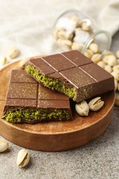 Photo of Pieces of Dubai chocolate bar with pistachios and knafeh on grey table, closeup