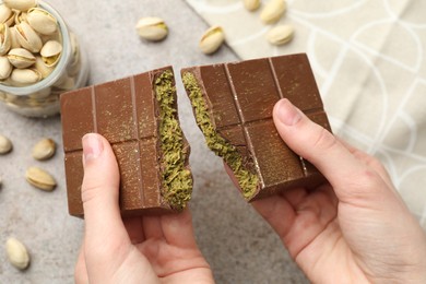 Photo of Woman breaking Dubai chocolate bar with pistachios and knafeh at grey table, closeup