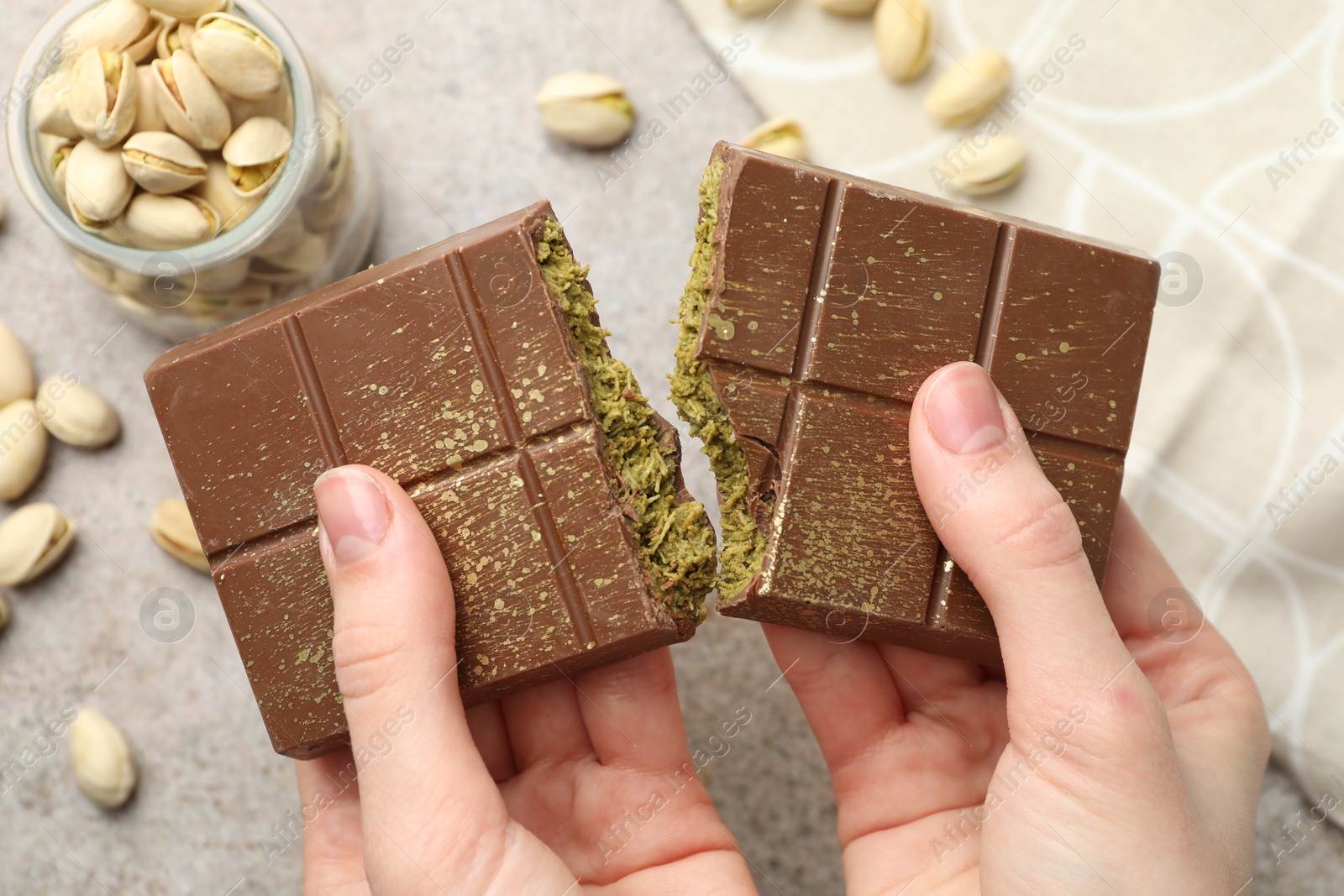 Photo of Woman breaking Dubai chocolate bar with pistachios and knafeh at grey table, closeup