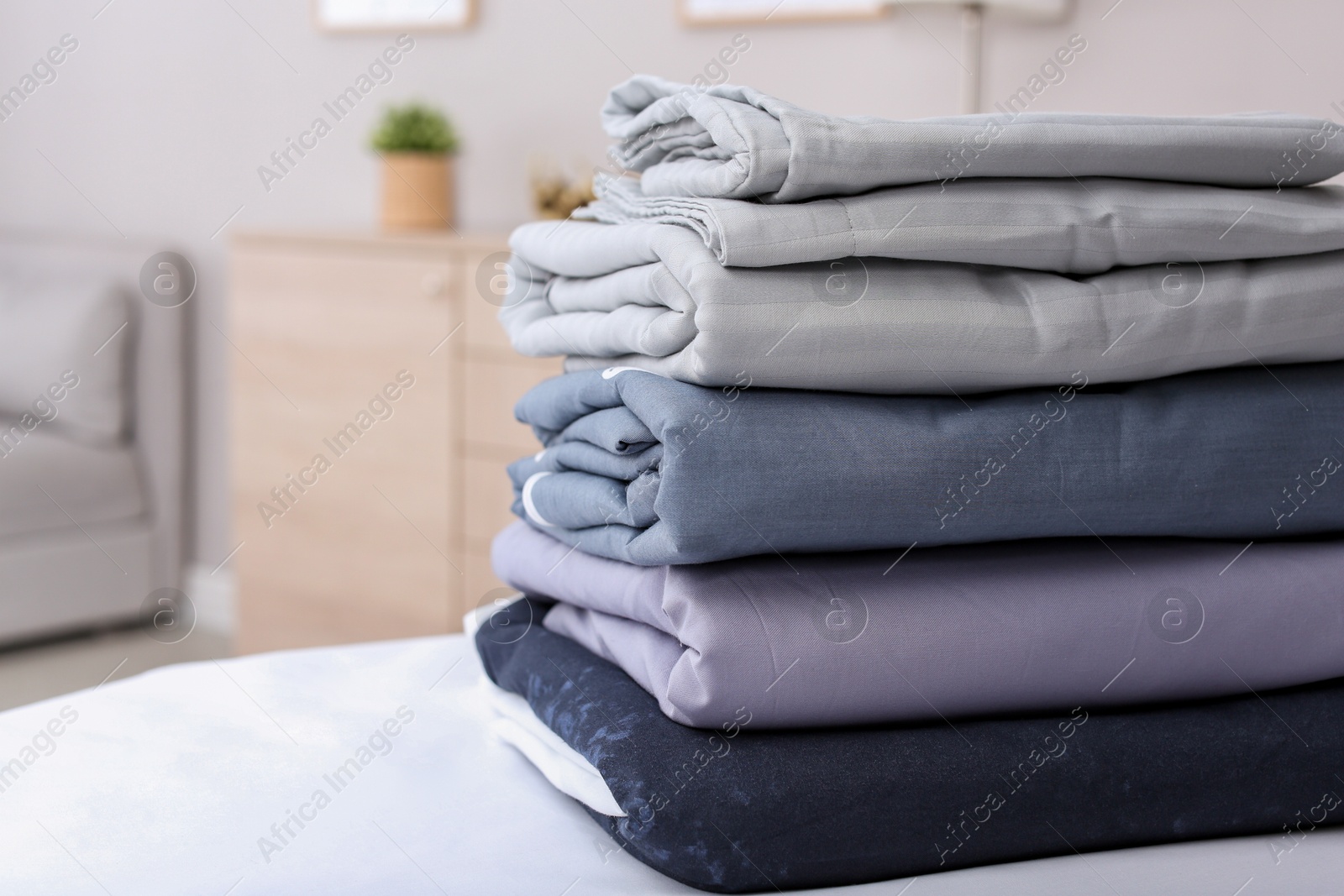 Photo of Stack of clean bed linens on table in room. Space for text