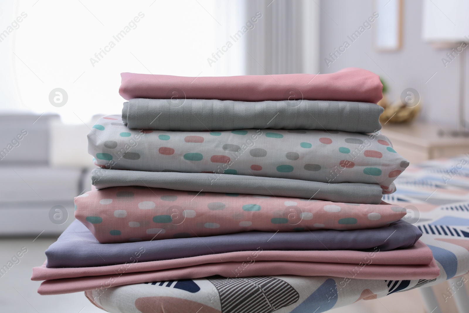 Photo of Stack of clean bed linens on ironing board in room