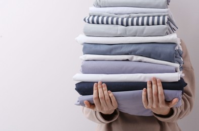 Photo of Woman holding stack of clean bed linens on light grey background