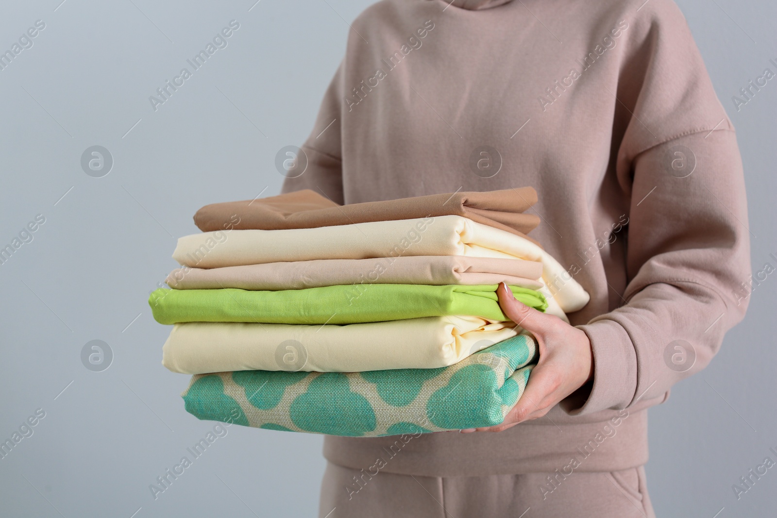 Photo of Woman holding stack of clean bed linens on light background, closeup