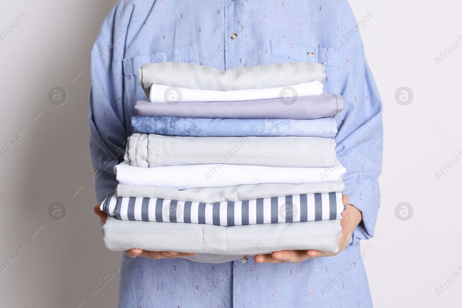 Photo of Woman holding stack of clean bed linens on white background, closeup