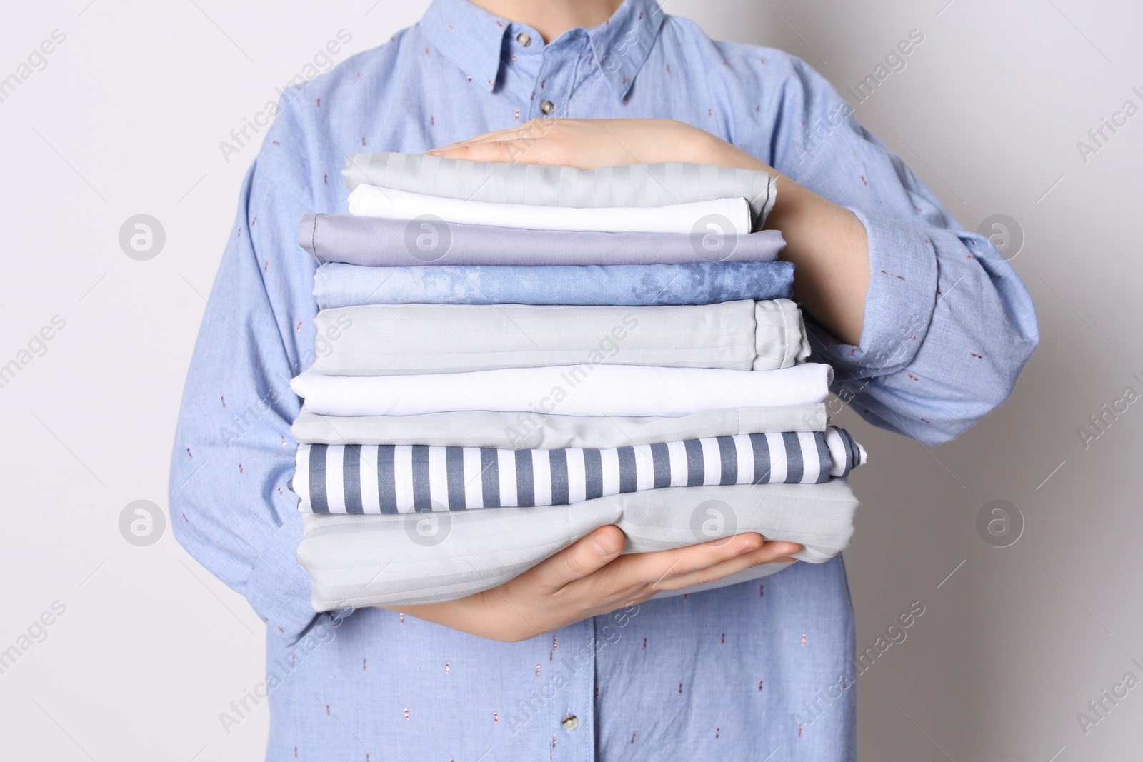 Photo of Woman holding stack of clean bed linens on white background, closeup