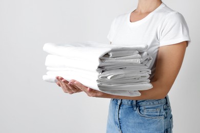 Photo of Woman holding stack of clean bed linens on light grey background